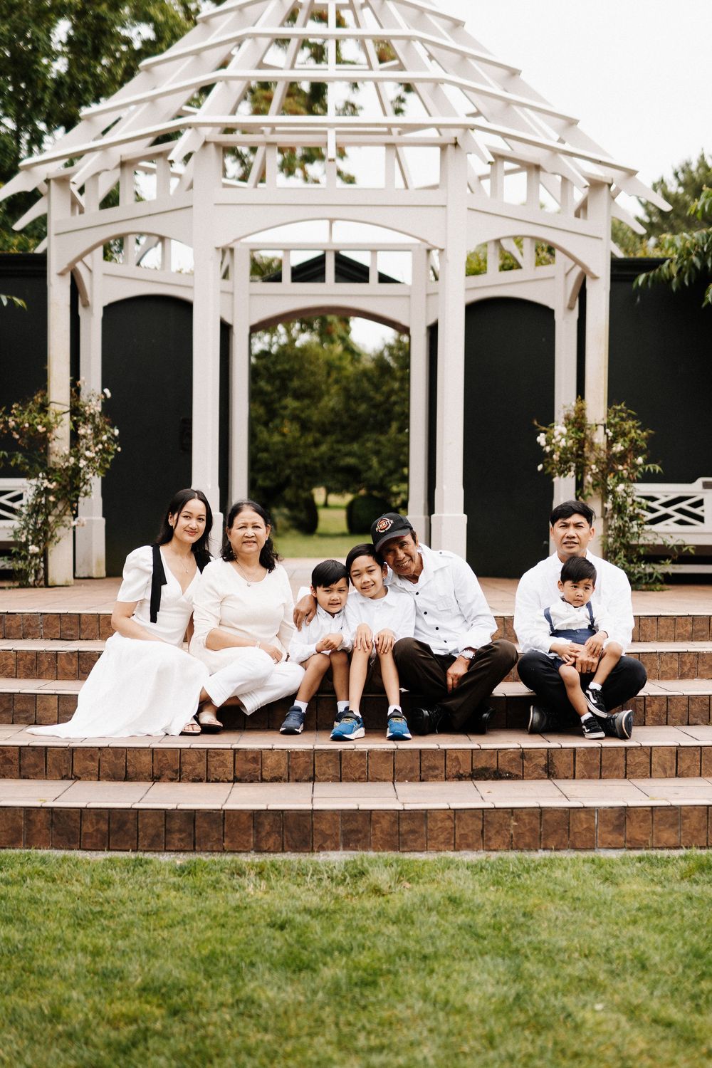 Group relaxing and lounging on steps beneath a white garden gazebo on a sunny day.