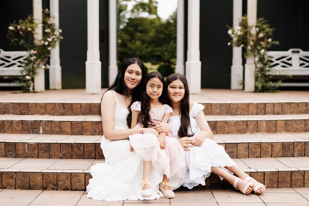 People in white dresses sitting and posing on brick stairs of a gazebo for a group photo.