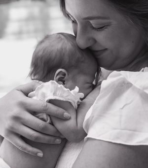 Black and white photo of a mother tenderly cradling her newborn baby close to her face.