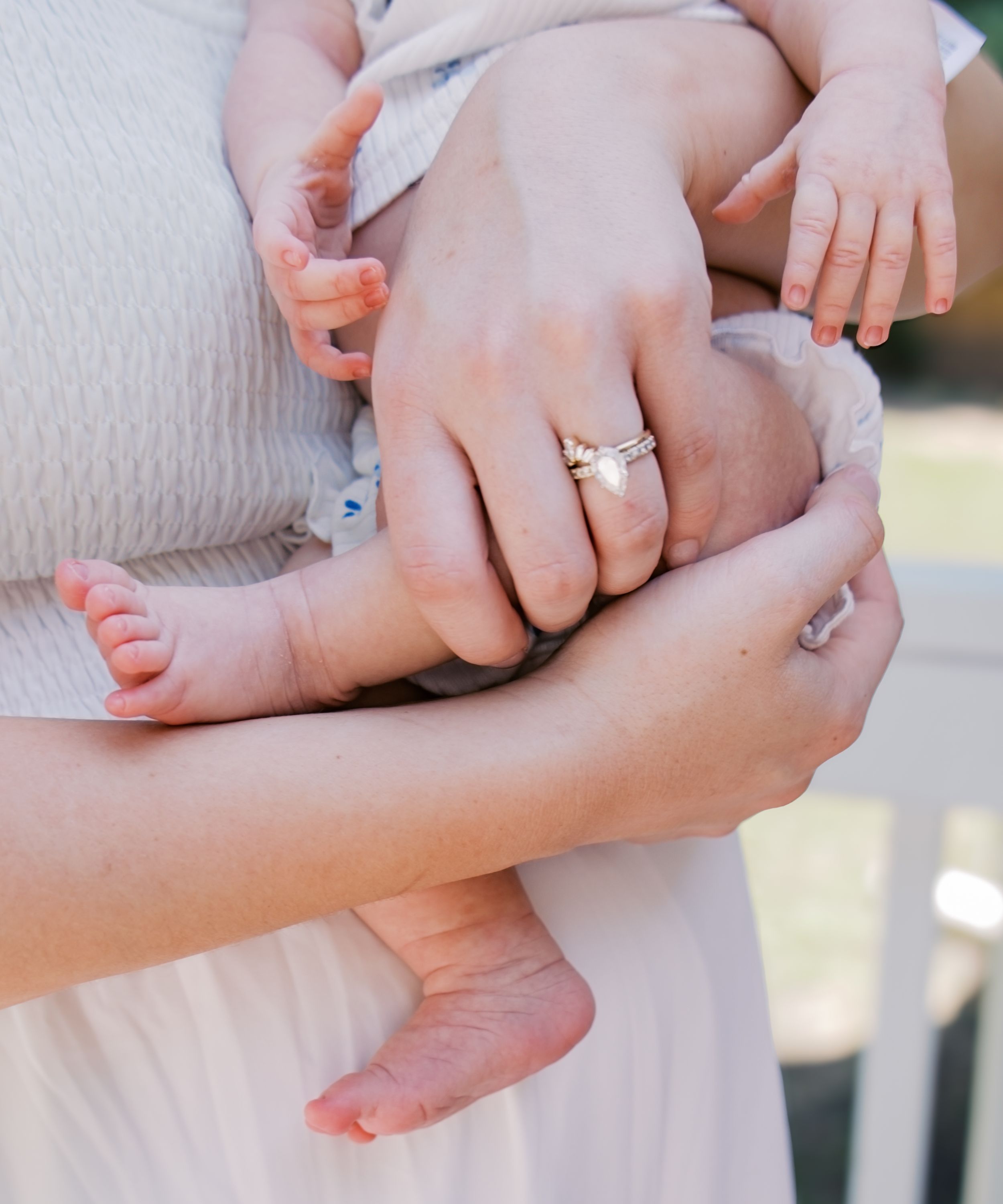 Close-up of tiny baby feet being held by gentle hands with an engagement ring.