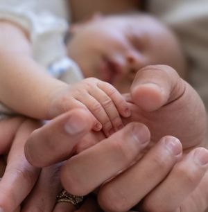 Extreme close-up of a tiny newborn hand grasping an adult finger.