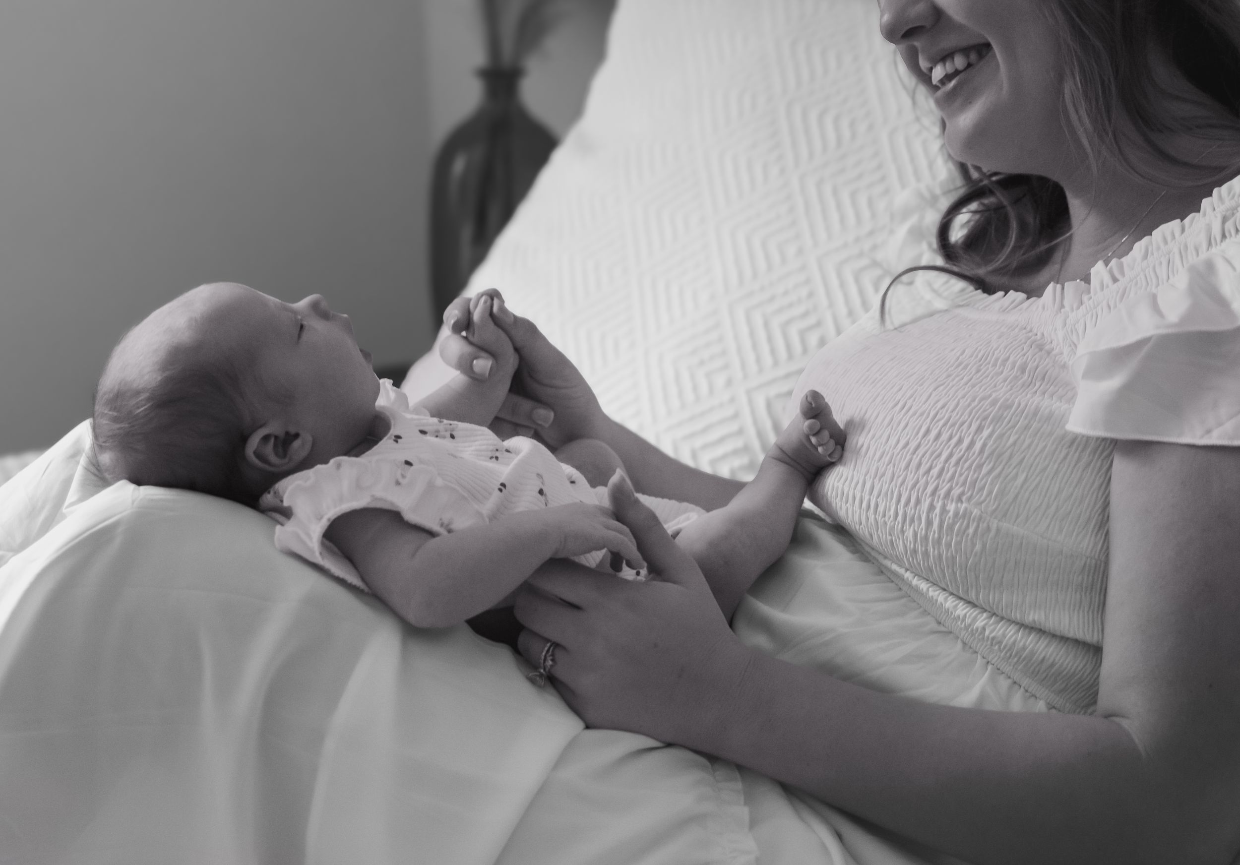 Black and white photo of a smiling mother cradling her newborn baby on a bed.