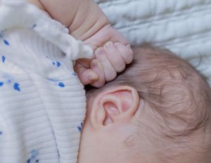 Close-up of a sleeping newborn baby's ear and tiny clenched fist resting on a soft white blanket.