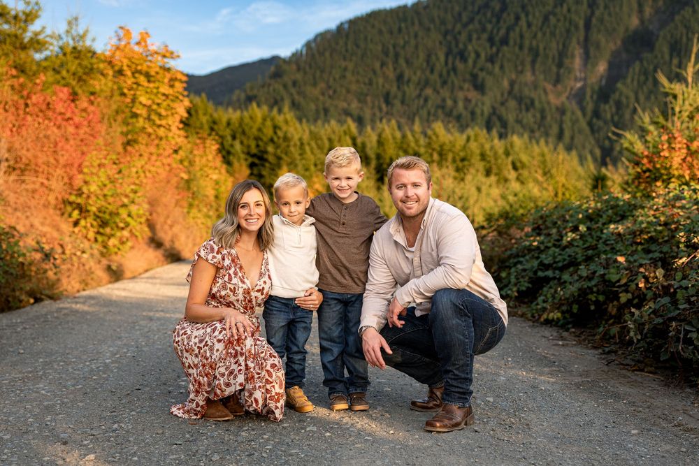 Family of four posing on a mountain road surrounded by vibrant autumn foliage in a scenic outdoor portrait.