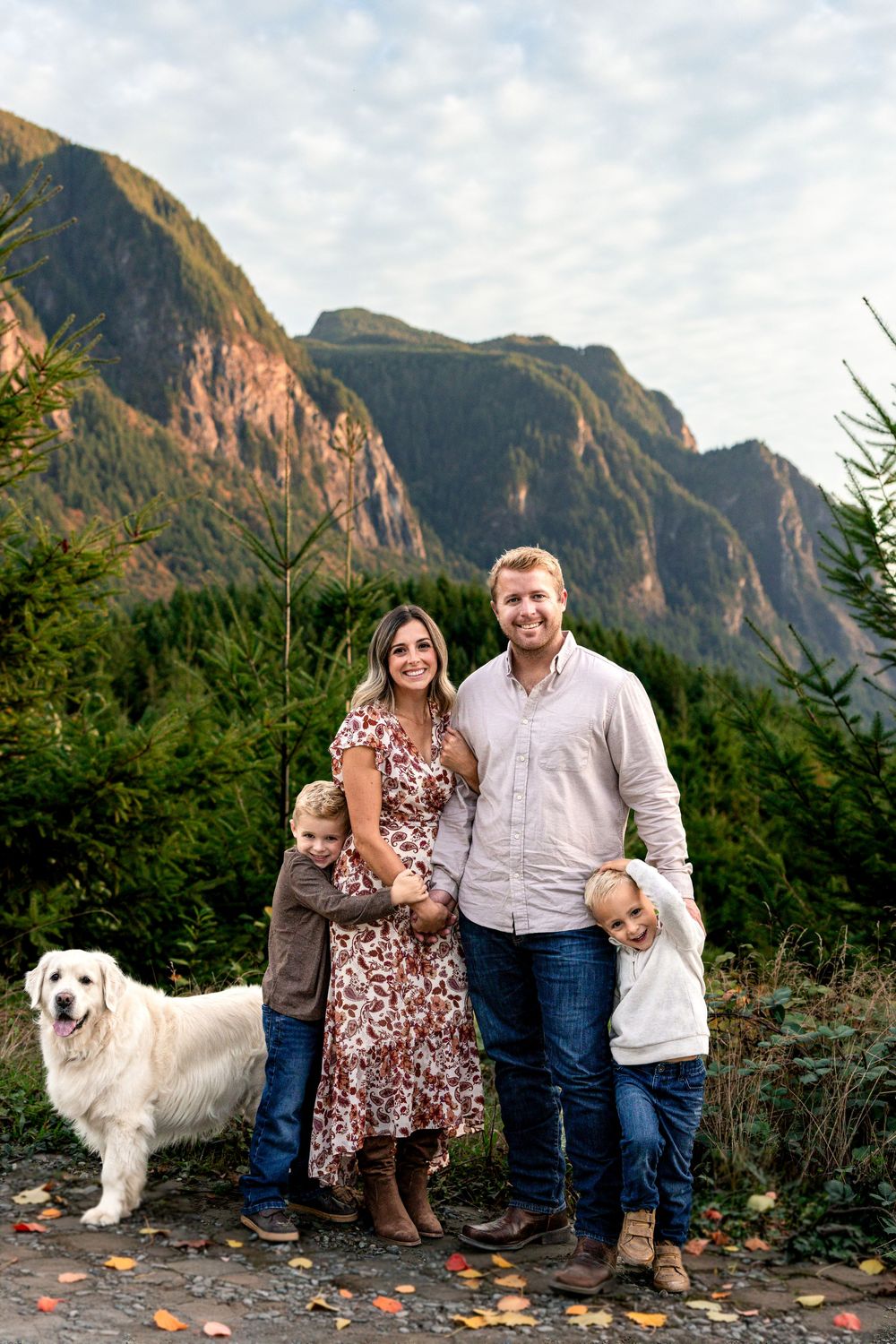 Family portrait with two boys and a white dog posing before a stunning mountain backdrop.