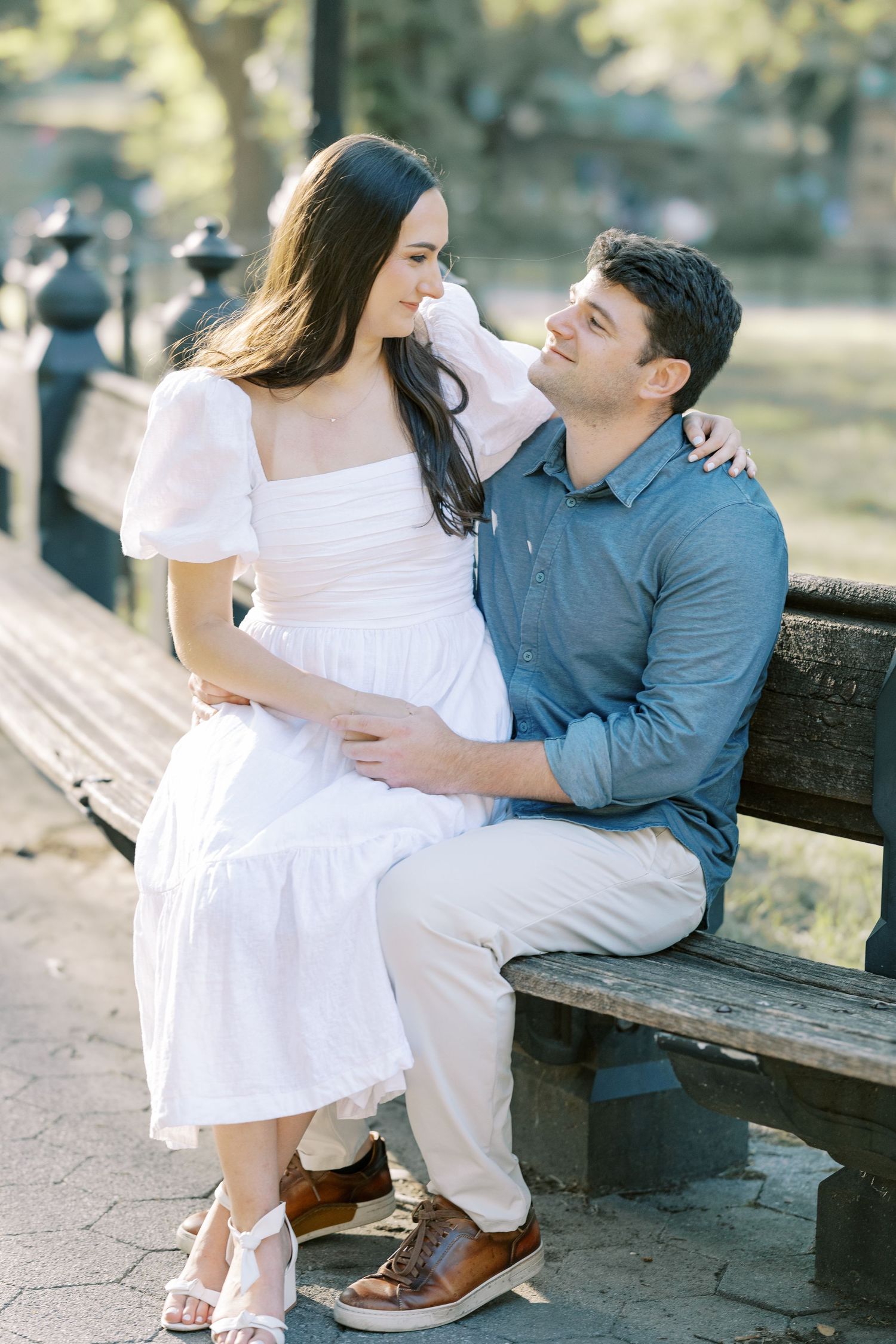 A couple shares an intimate moment while sitting together on a park bench during an outdoor photo session.