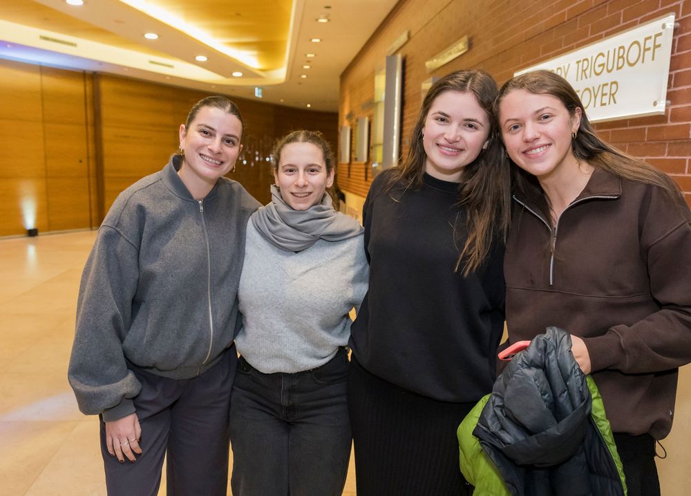 Four students gather for a casual group photo in a warmly lit indoor hallway.