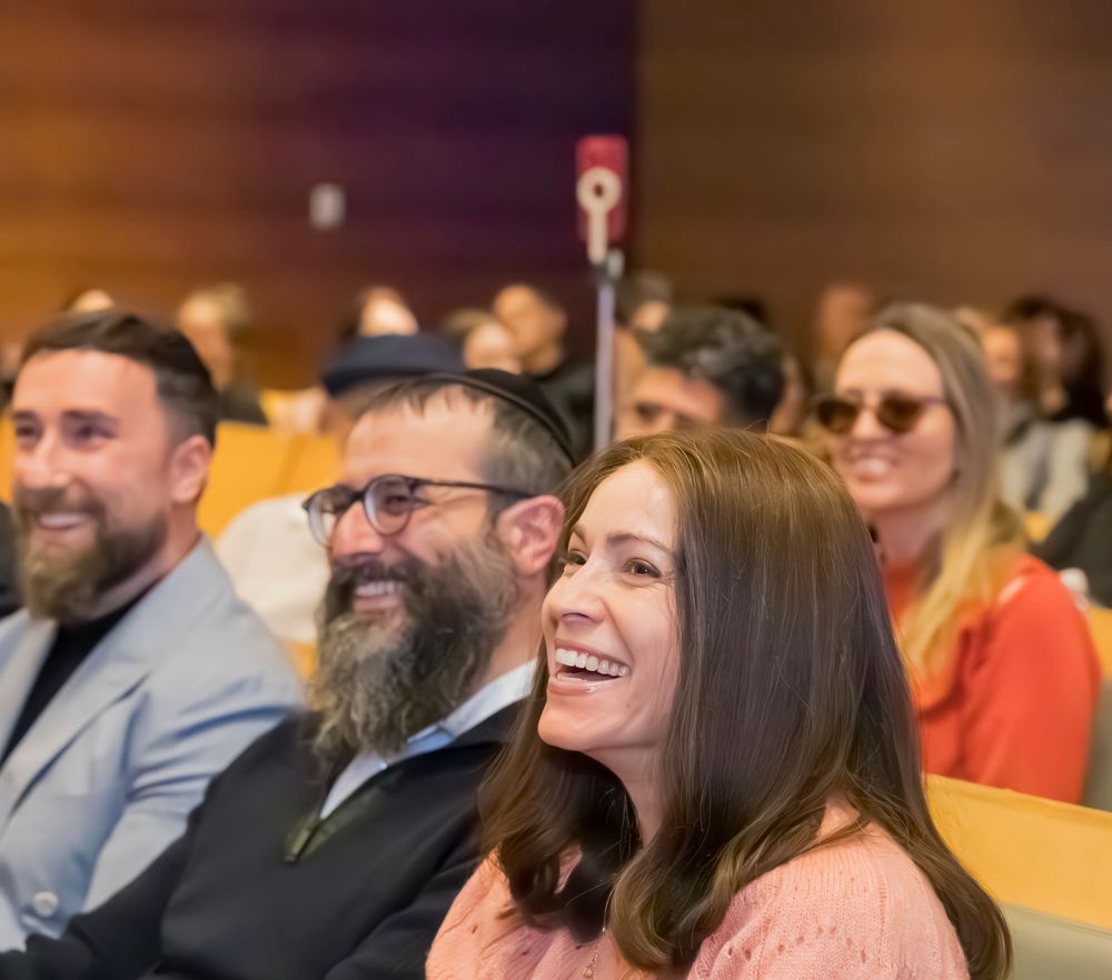 Audience members smile and laugh while seated in auditorium seats during an event.