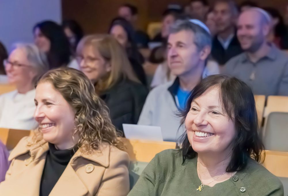 Conference attendees smiling and engaging during a presentation in a modern auditorium setting.