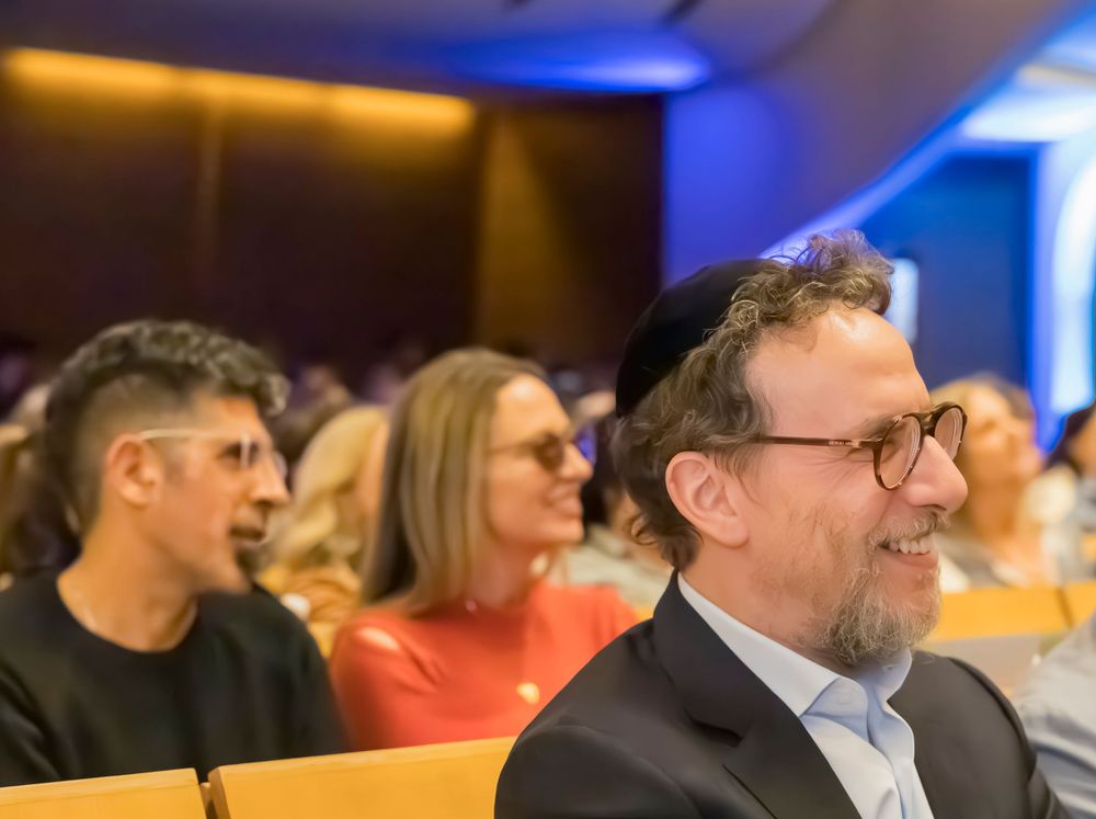 Audience members smile and engage during a professional conference or event with warm lighting and blue accents.