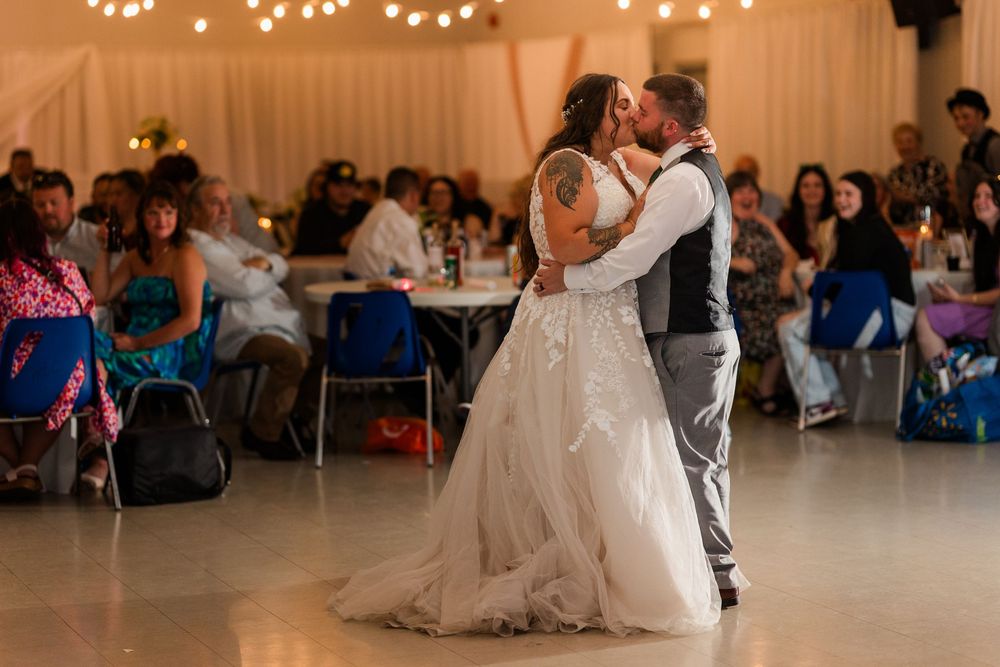 A romantic first dance moment between newlyweds at their wedding reception with guests watching in the background.