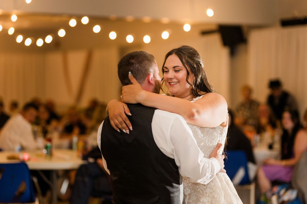 A romantic first dance moment at a wedding reception with string lights and tables in the background.