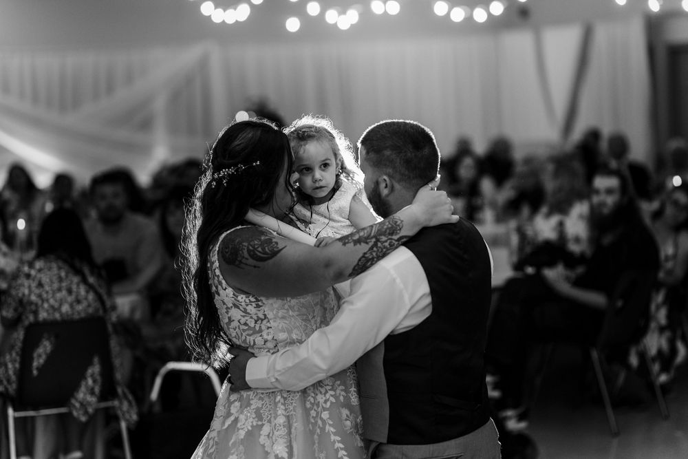 A couple shares a romantic slow dance together on a wedding reception dance floor under glowing lights.