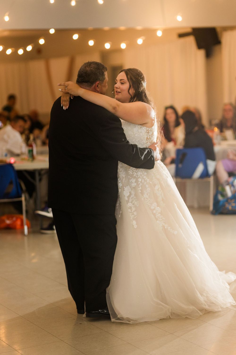 A couple shares a romantic dance at their wedding reception with twinkling lights in the background.