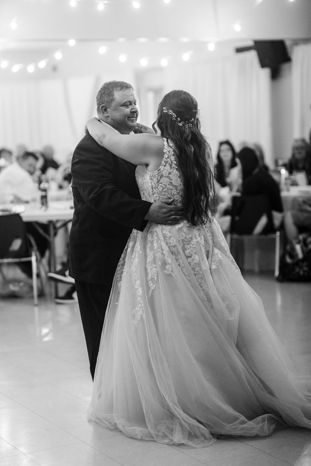 A couple shares their first dance at a wedding reception under string lights in a white tent.