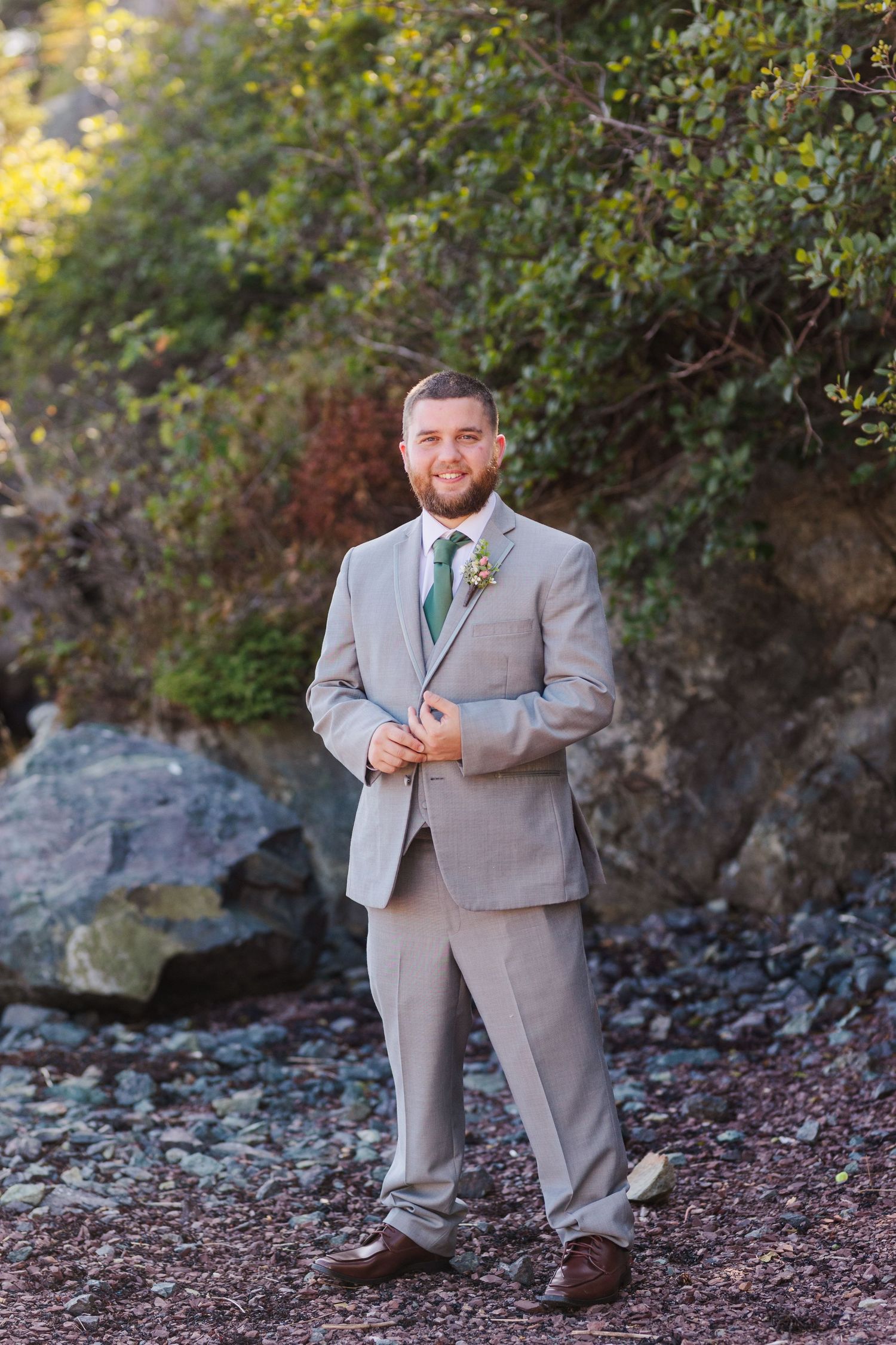 Person in light gray suit with green tie stands by rocky cliff side on beach during golden hour.
