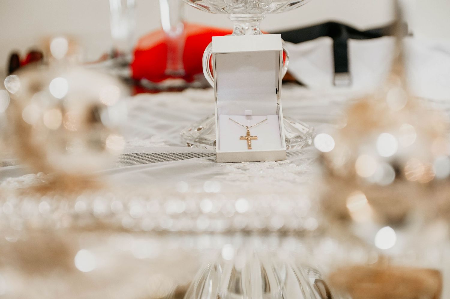 White wedding ring box sits on a formal table setting with bokeh lights and glassware in the background.