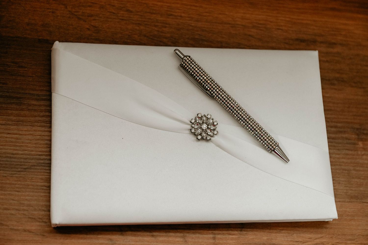 An ornate silver feather bookmark rests diagonally across a folded white paper napkin on a wooden table surface.