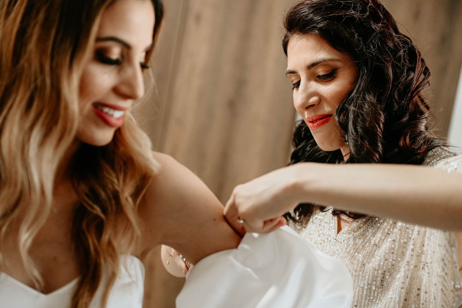 Two smiling people with wavy hair examine a white wedding dress in a candid behind the scenes moment.