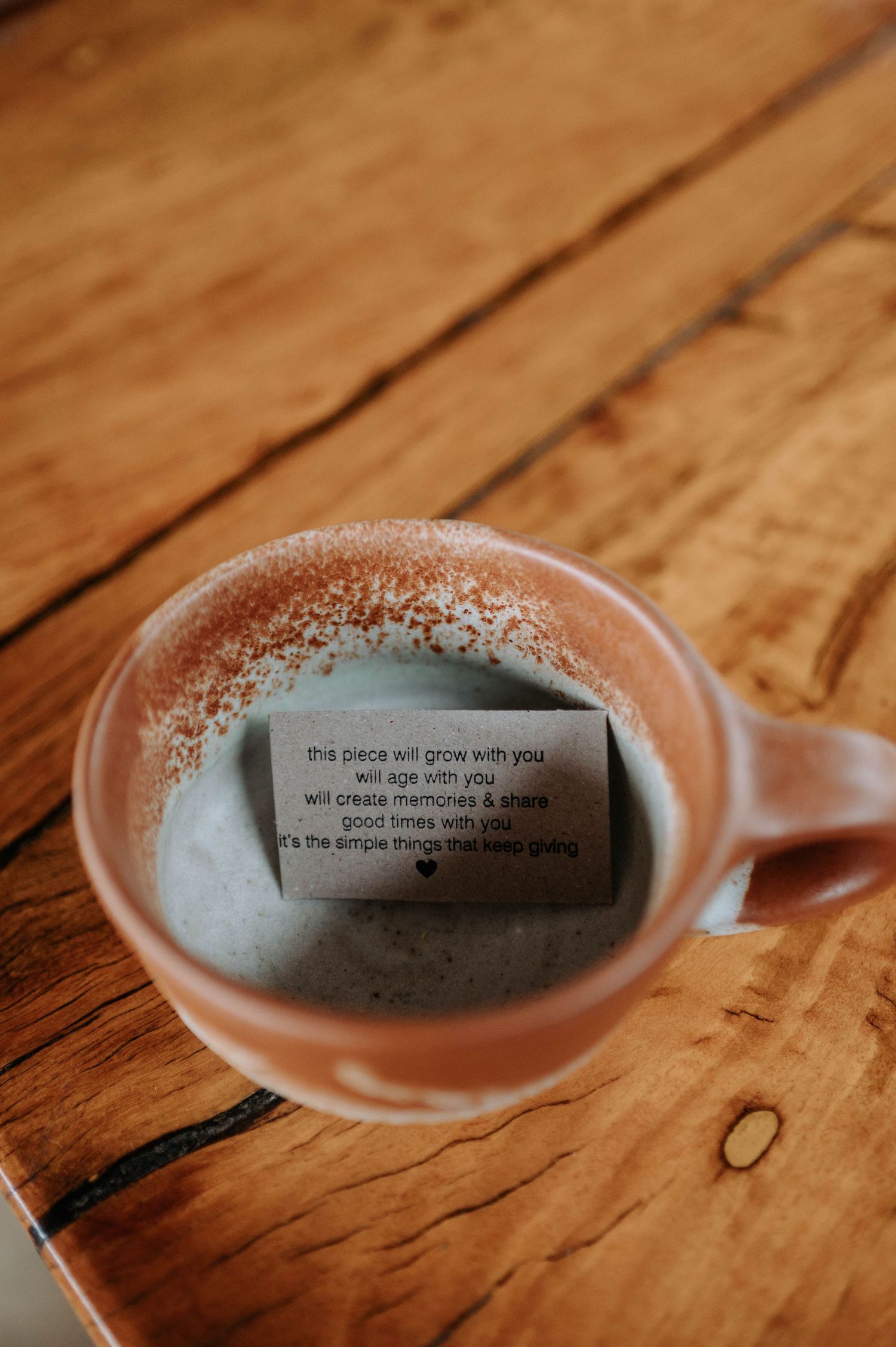 A paper fortune or message sits inside a white ceramic mug on a wooden table surface.
