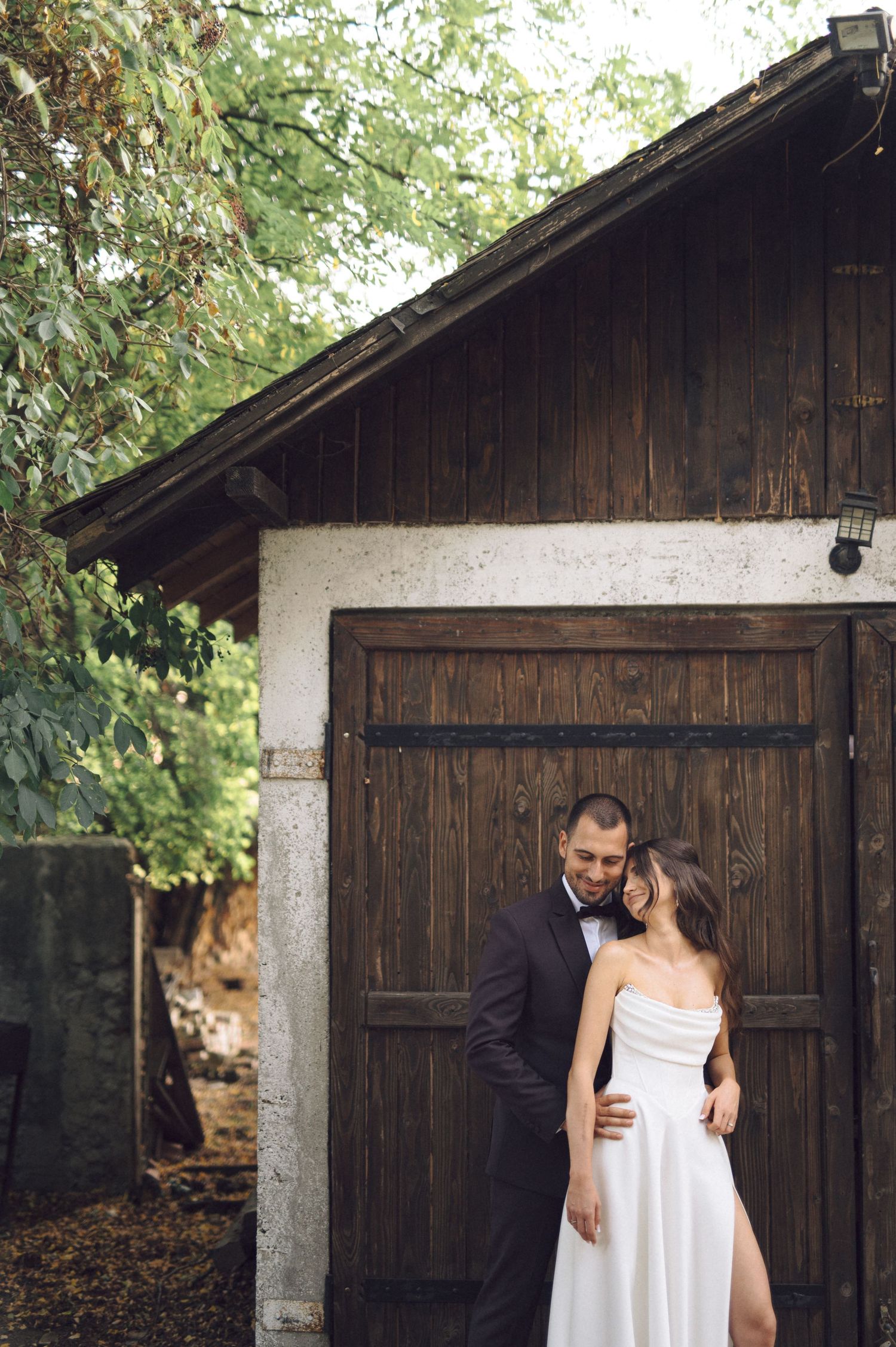 A couple in wedding attire poses intimately against a rustic wooden barn backdrop.