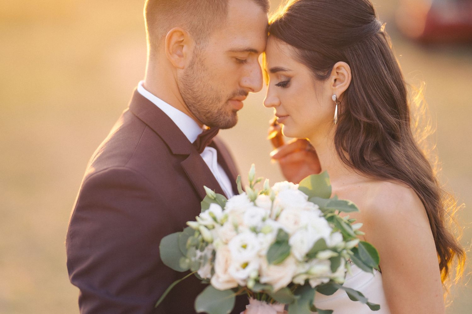 Romantic couple embraces during golden hour sunset wedding photoshoot in an outdoor field.