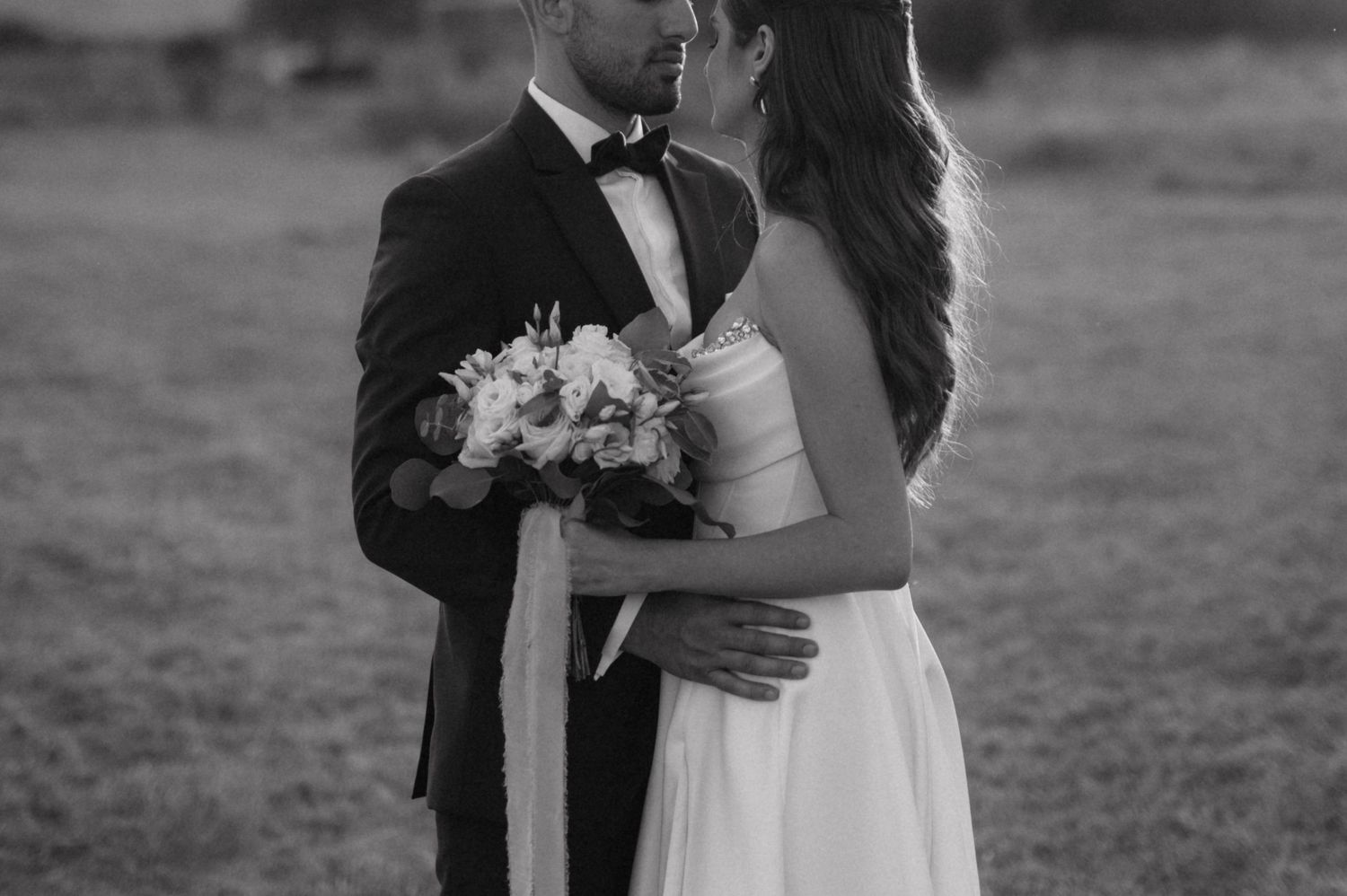 A romantic newlywed couple share kisses in a black and white photo series taken in an outdoor setting.