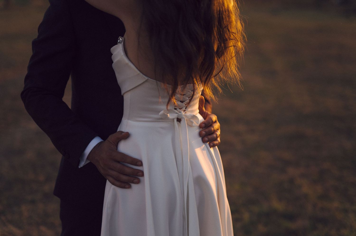 Newlyweds share an intimate moment in warm sunset lighting with white floral bouquet.