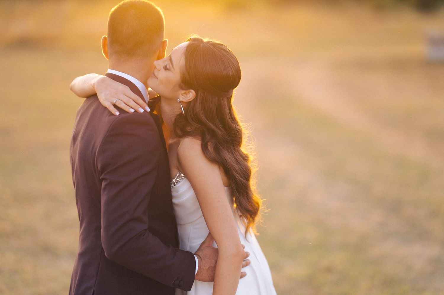 Wedding couple poses in soft golden sunlight with bride holding delicate white bouquet.