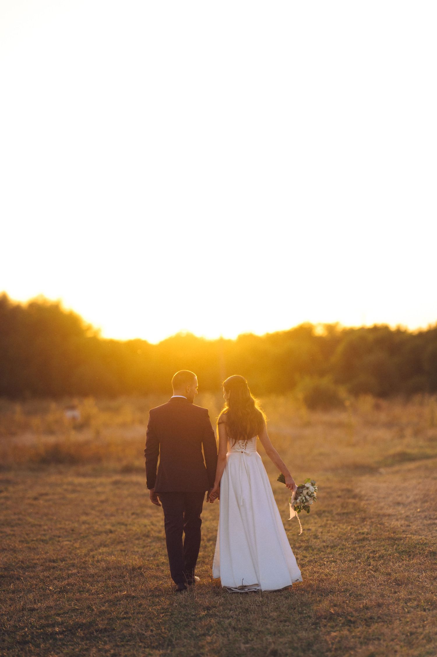 A couple walks together during golden hour sunset in a desert landscape with warm glowing light.