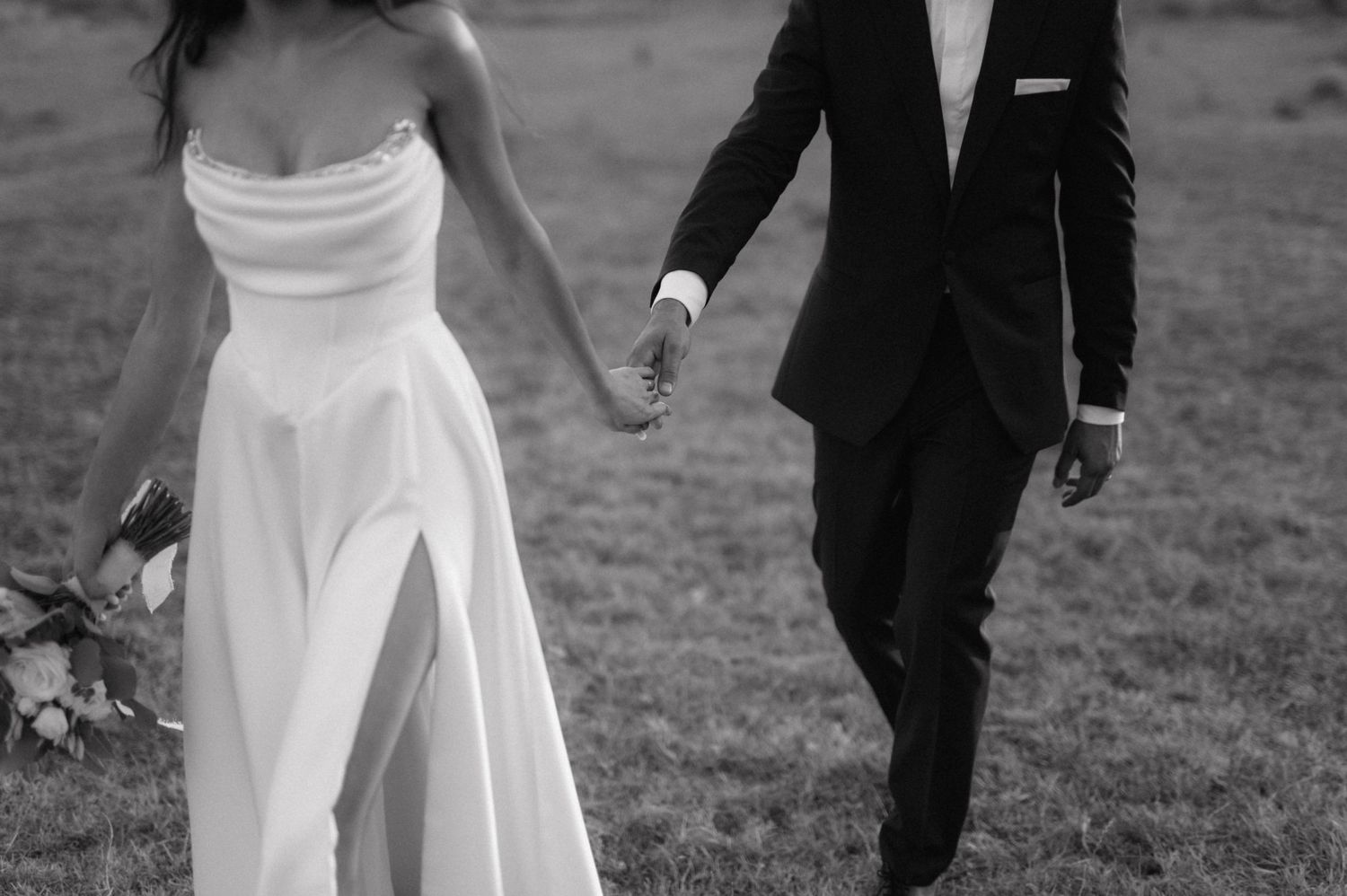 A bride and groom share a playful dance together in a grassy outdoor field.