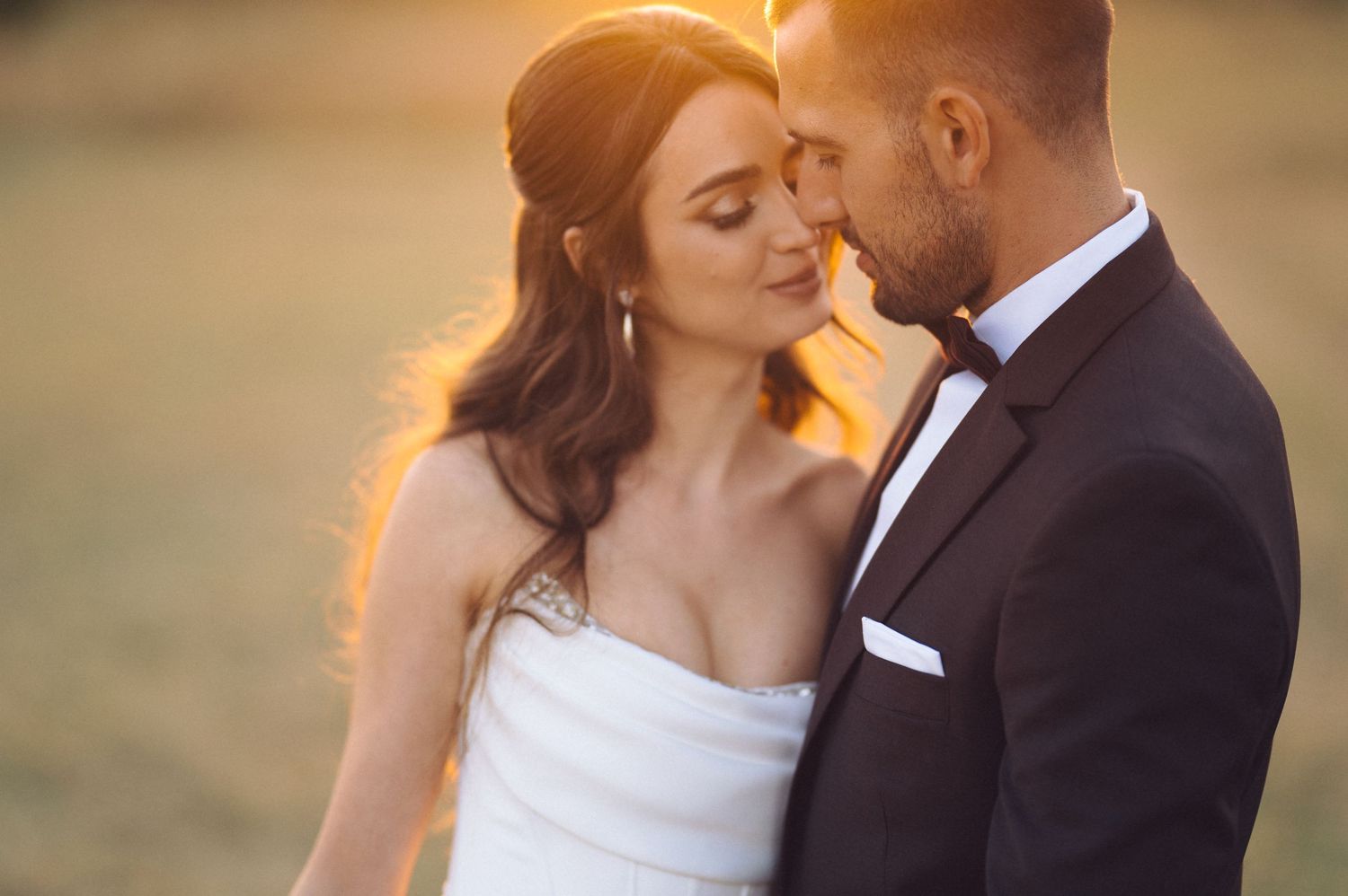 Wedding couple embraces in romantic outdoor setting at sunset with golden light filtering through the trees.