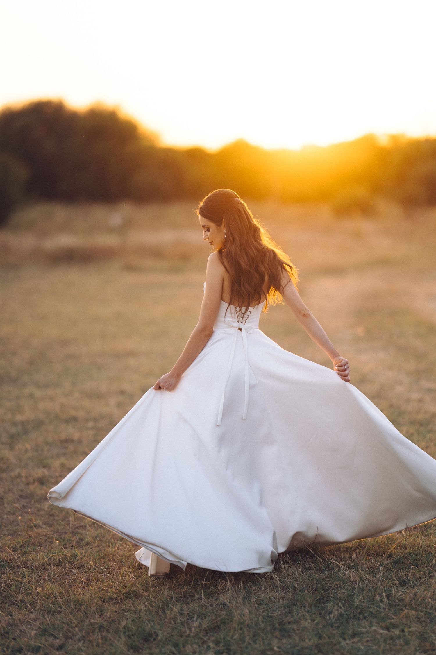 A woman in a flowing white dress twirls gracefully in a sunlit field during golden hour.
