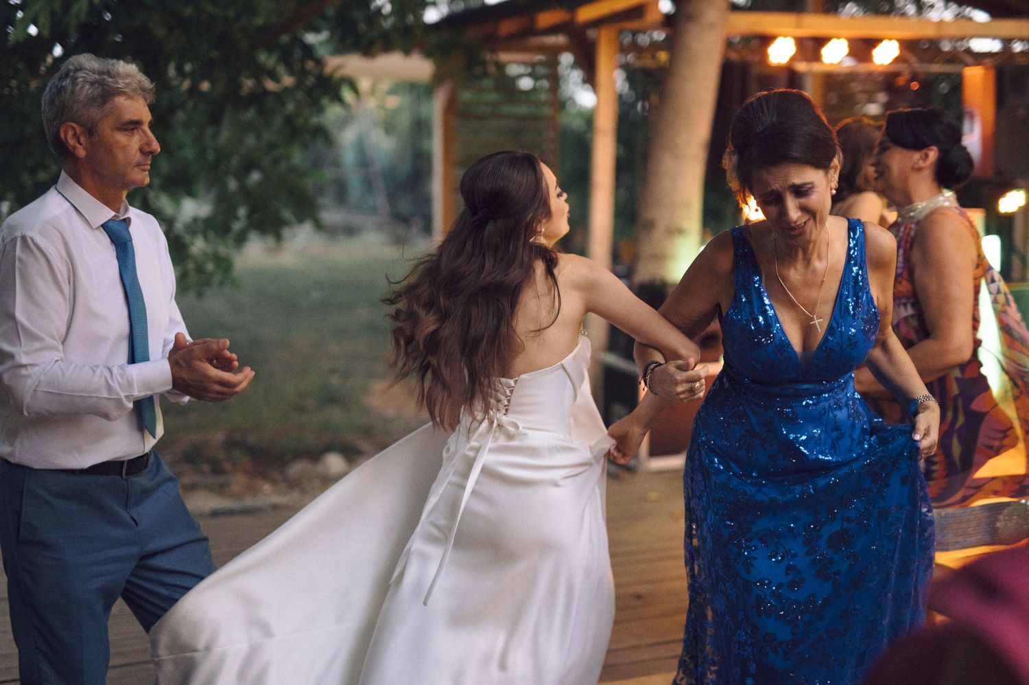 A wedding couple and their guests dance under string lights at an outdoor evening reception.