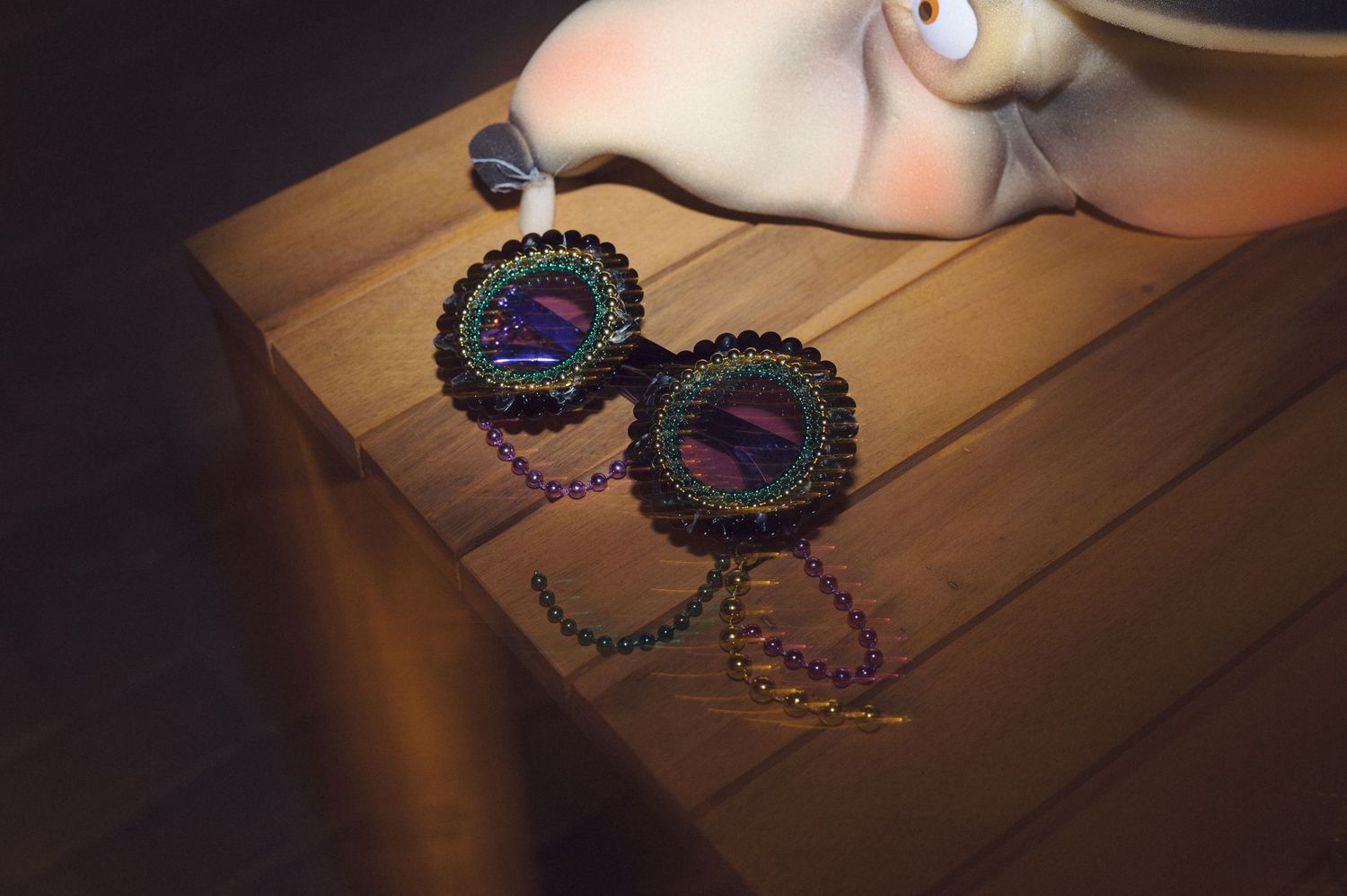 Colorful beaded pine cone ornament catching light on wooden table reflecting sparkly iridescent decorative details.
