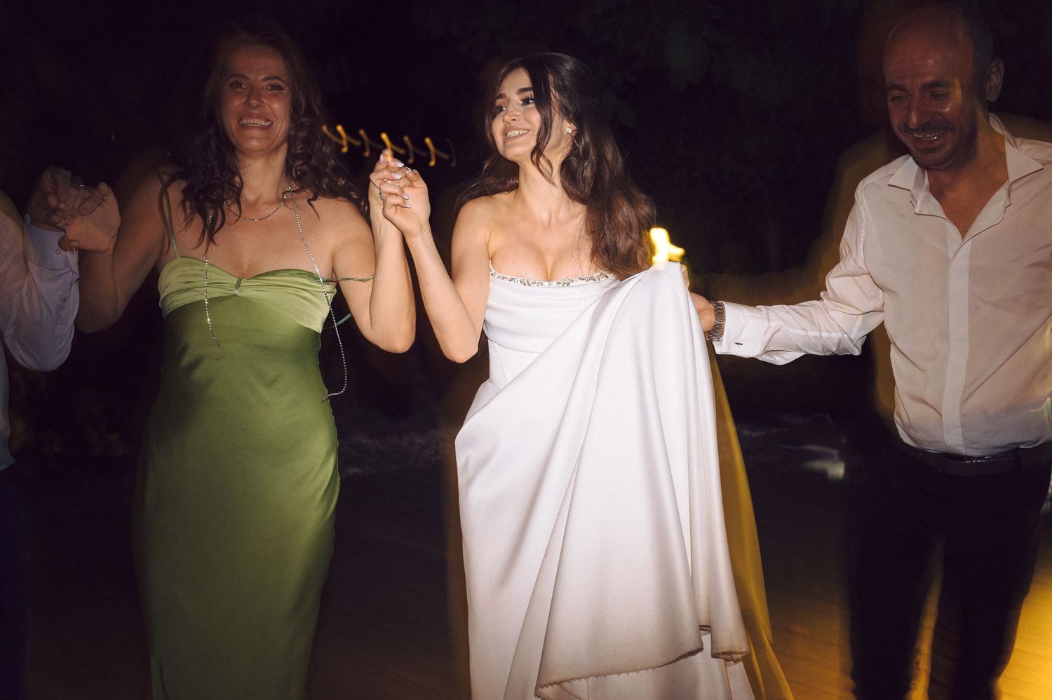 A group of people dancing at a dimly lit party or wedding reception.