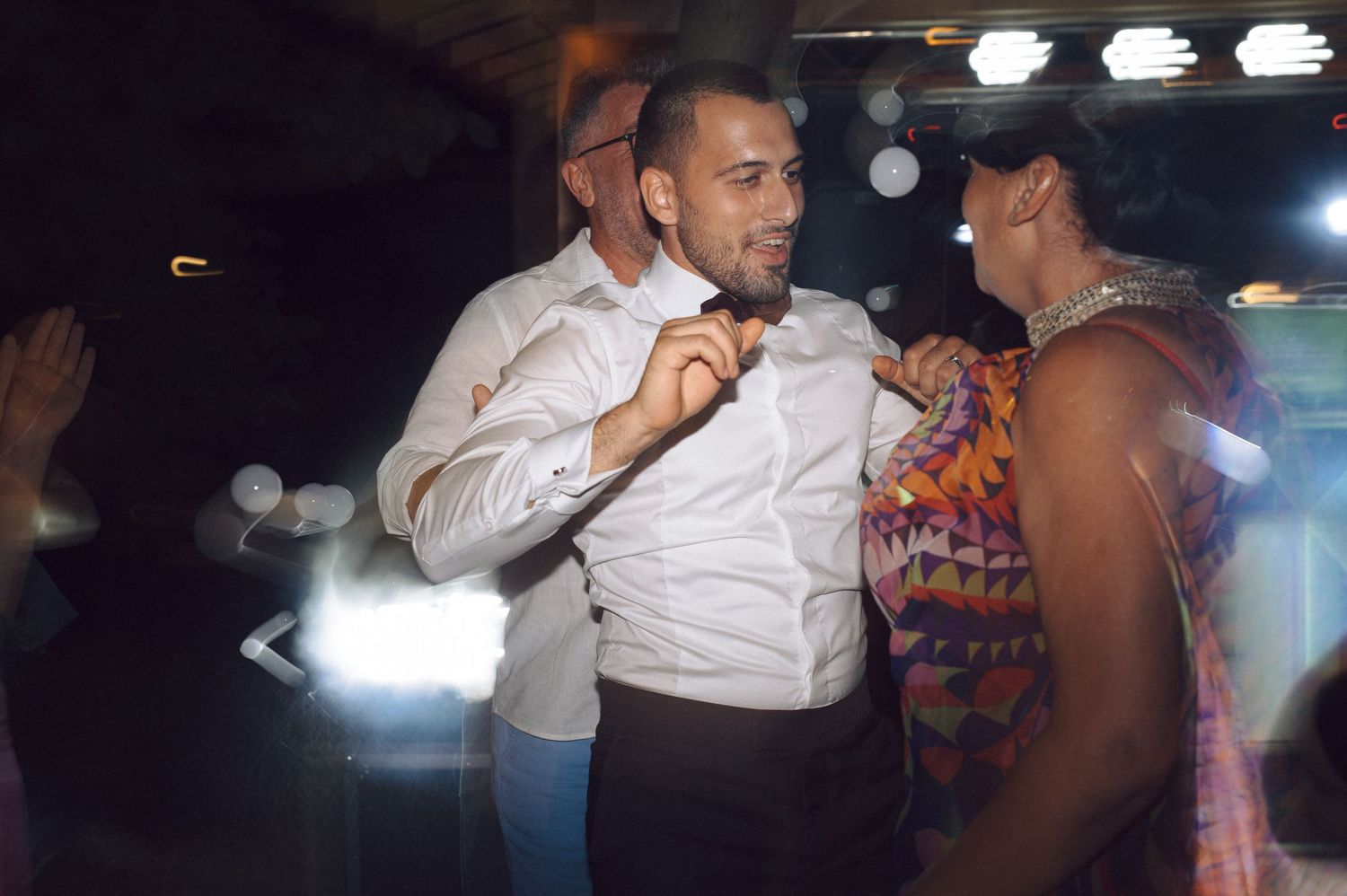 People dancing together in a dim nightclub setting with overhead lighting illuminating the dance floor.