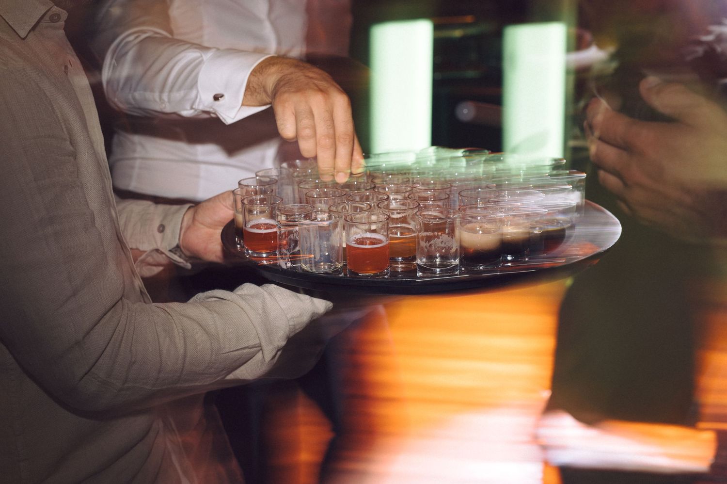 Close-up shot of hands pouring drinks at a dimly lit bar or restaurant setting.
