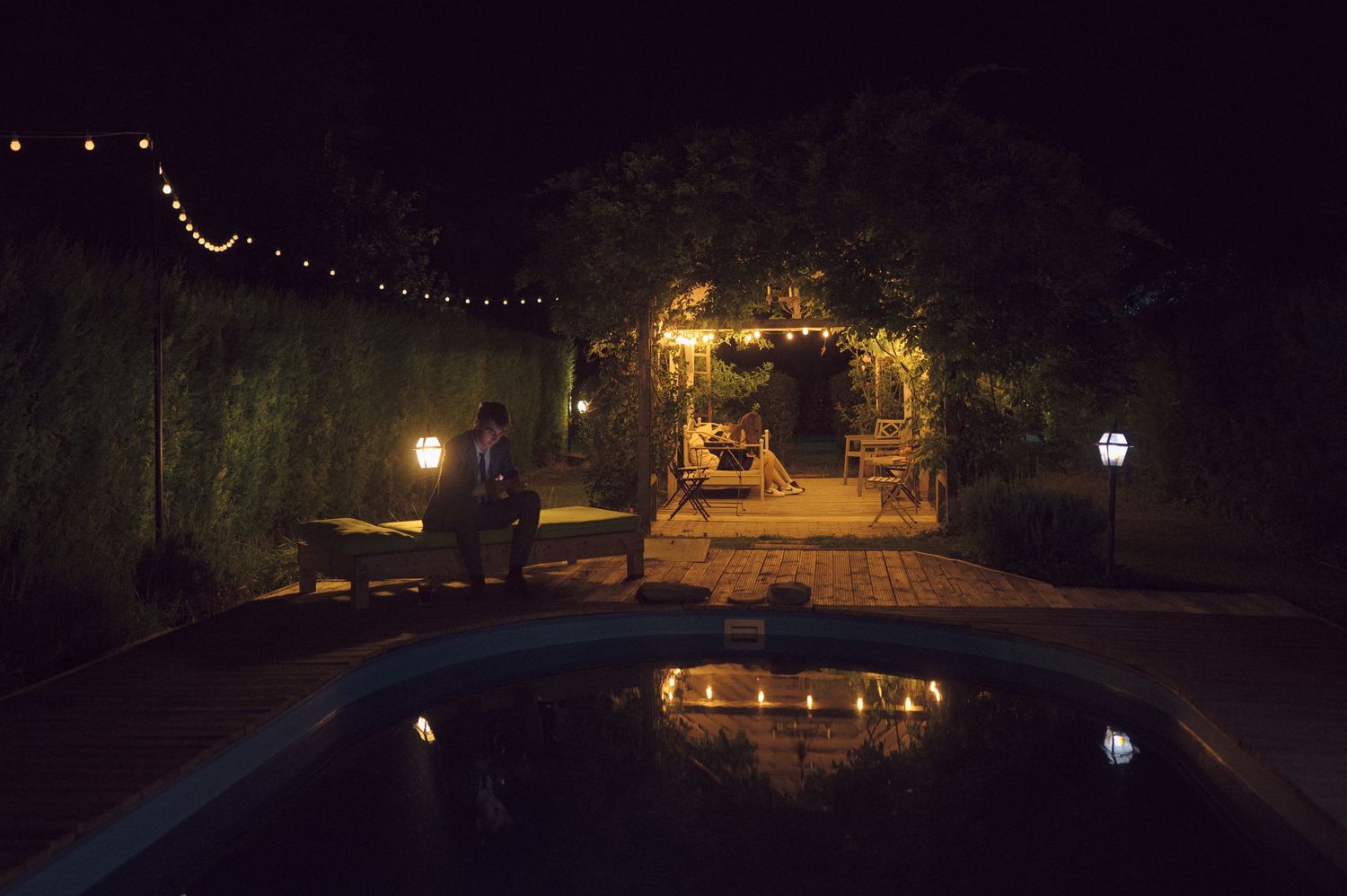 A romantic poolside setup with string lights and lanterns creating a magical nighttime ambiance.