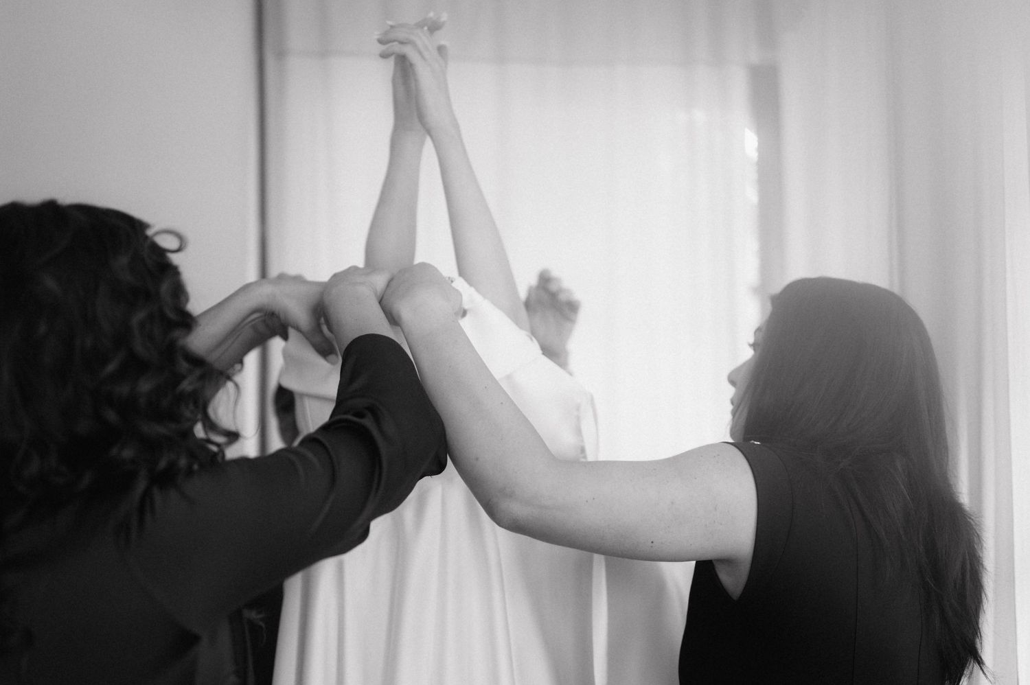 A sequence of black and white photos showing hands meeting and gently touching through a curtained window.