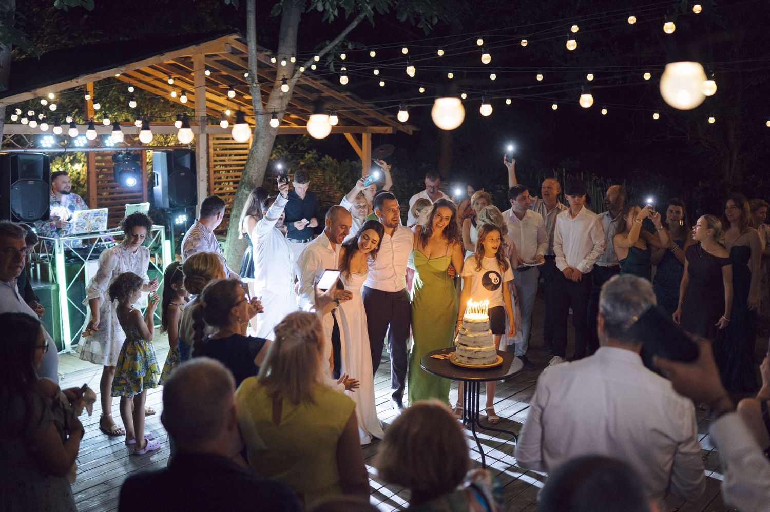 String lights and paper lanterns illuminate an outdoor evening wedding reception space with dancing guests.