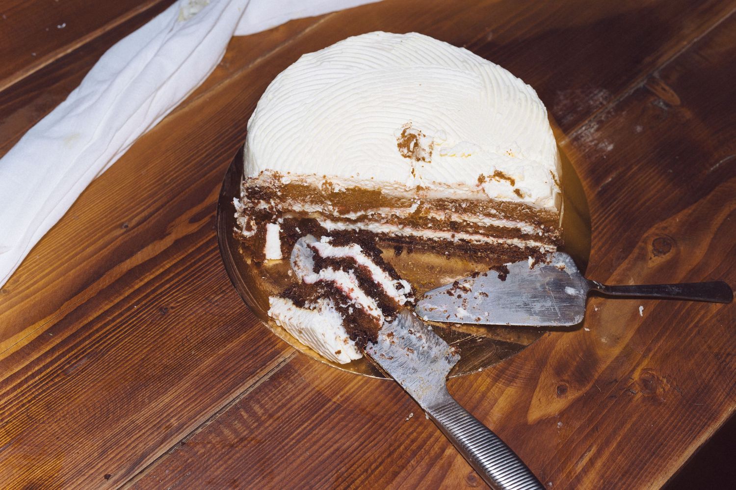A partly sliced chocolate layer cake with white frosting sits on a wooden surface with a knife beside it.