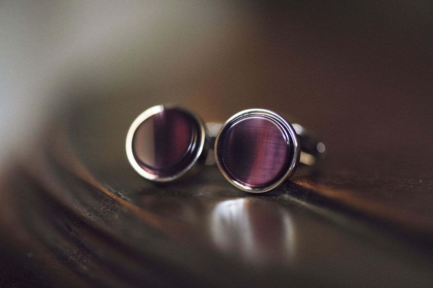 Silver wedding rings with reflective glare on dark wooden surface create dramatic lighting effect.