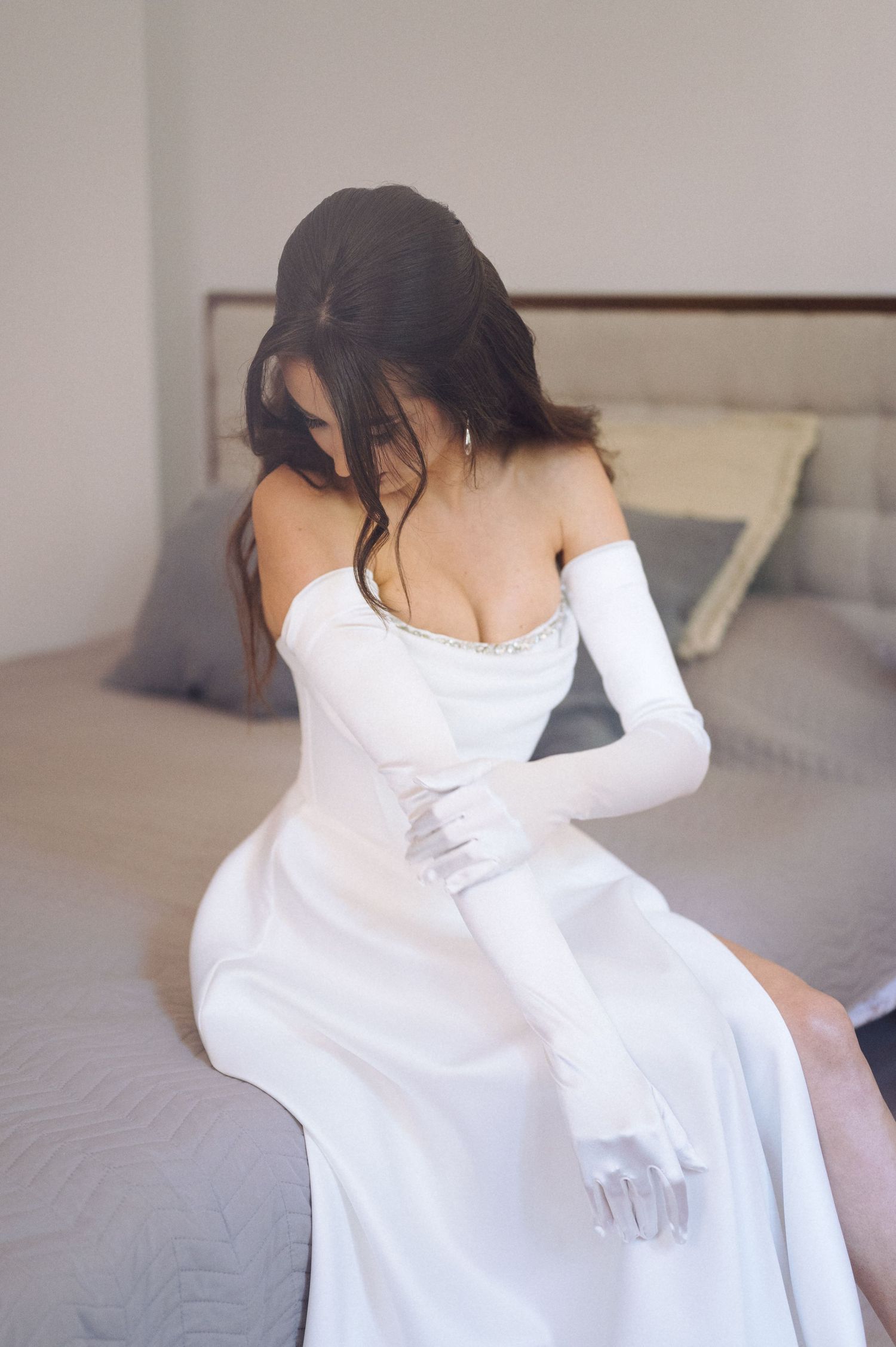 Person in white dress leans back against a light colored wall as their dark hair gracefully falls.