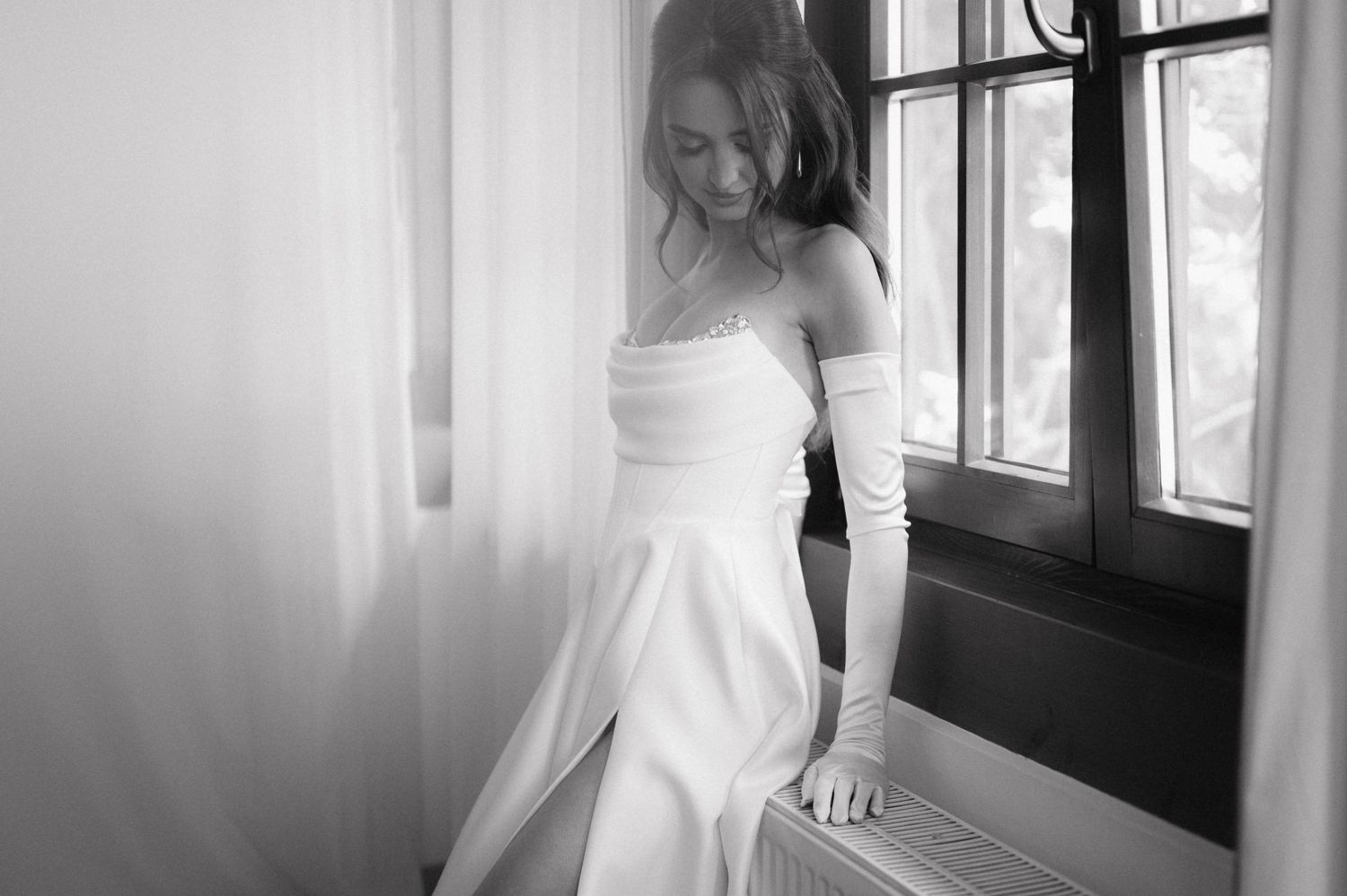 A series of black and white wedding photography images showing a bride in a white dress near window lighting.