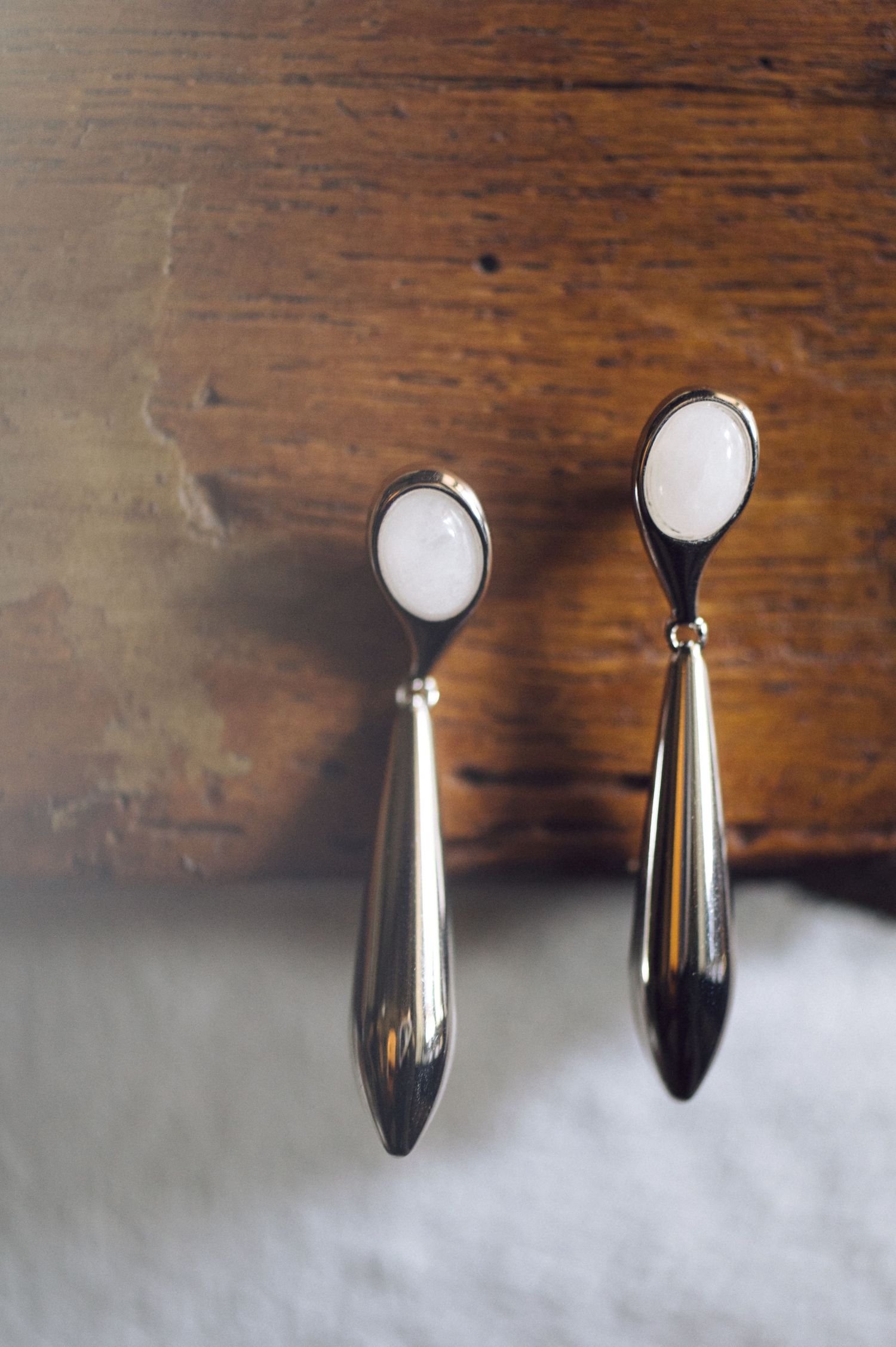 Small metal spoon with liquid on its rounded silver surface casting reflection on dark wood background.