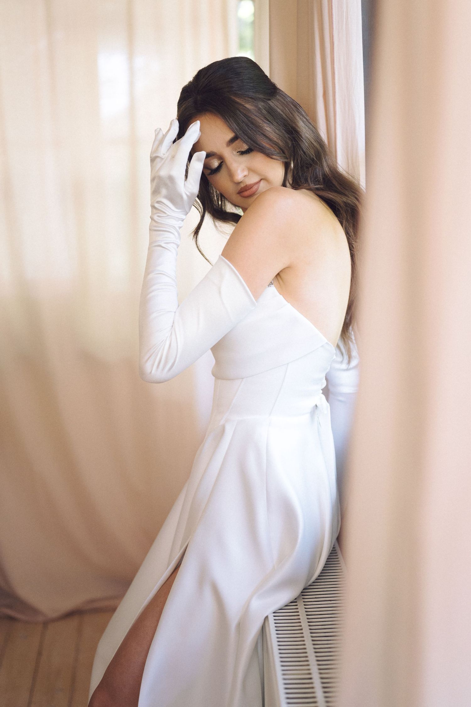 Woman in a flowing white long-sleeved dress poses gracefully in soft natural lighting.