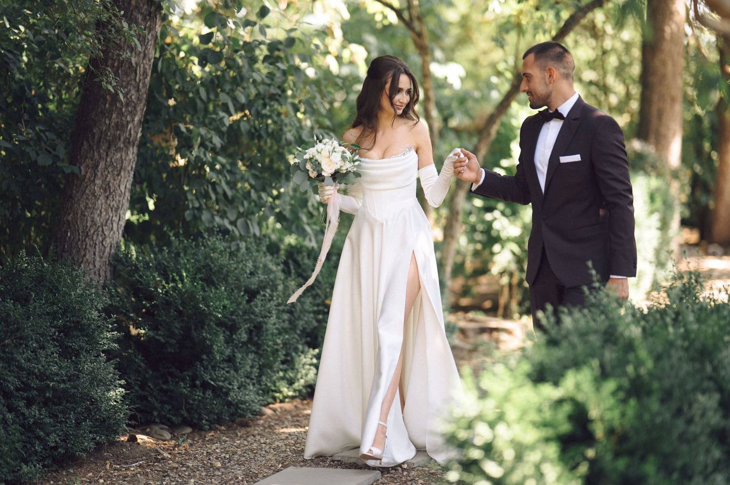 A romantic wedding couple shares intimate moments in a lush garden setting under natural sunlight.