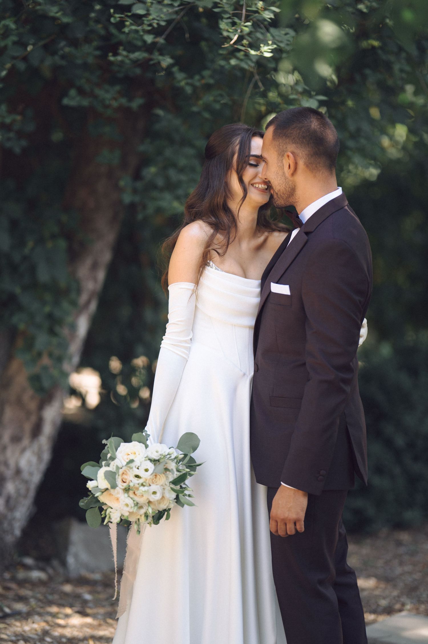 Newlywed couple shares romantic kisses in a series of intimate outdoor wedding photos with green foliage backdrop.