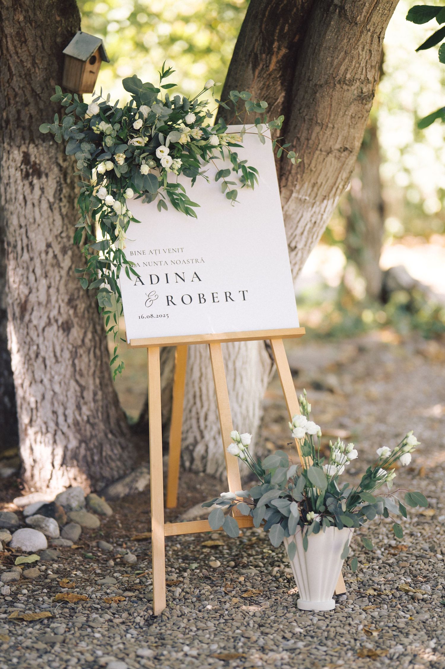 Four rustic wooden easels with white name cards decorated with eucalyptus leaves create an elegant outdoor wedding display.